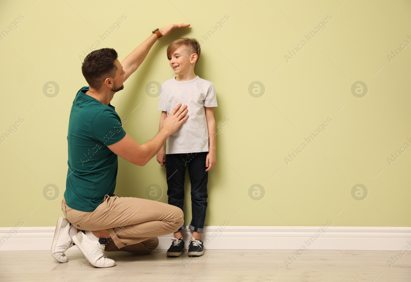 Photo of Father measuring height of his son near light wall indoors. Space for text