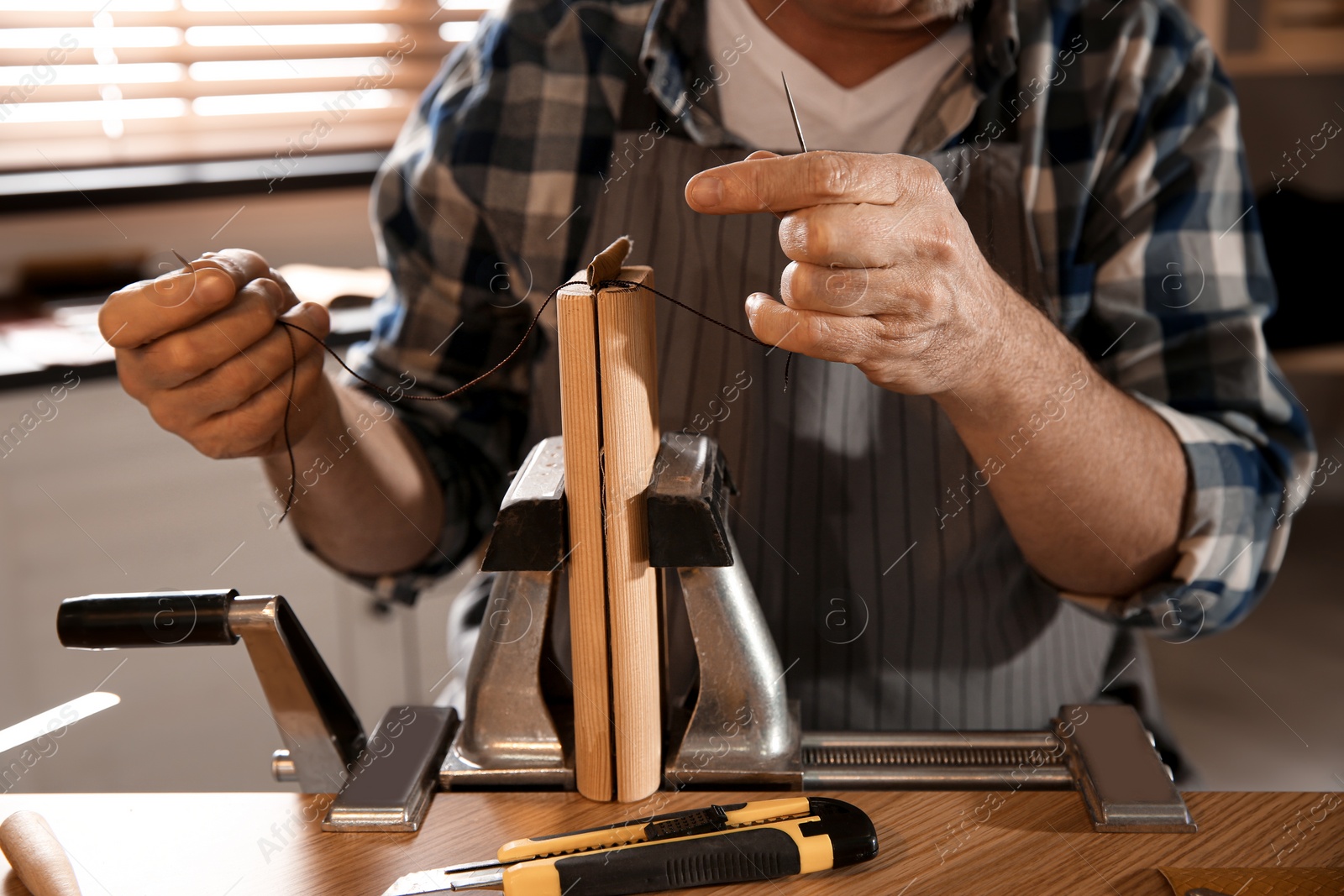 Photo of Man sewing piece of leather in workshop, closeup