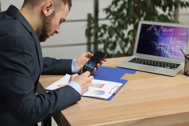 Photo of Forex trader working with smartphone and charts at table in office