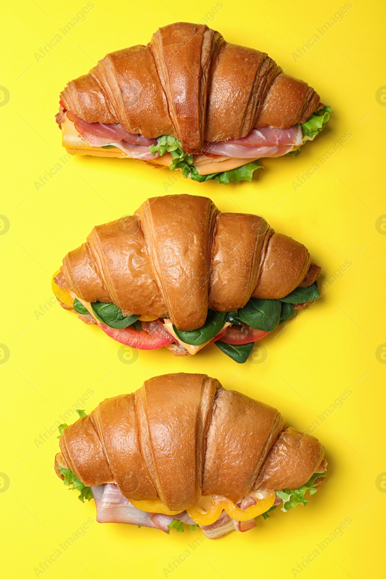 Photo of Tasty croissant sandwiches on yellow background, flat lay