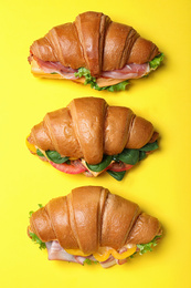 Tasty croissant sandwiches on yellow background, flat lay