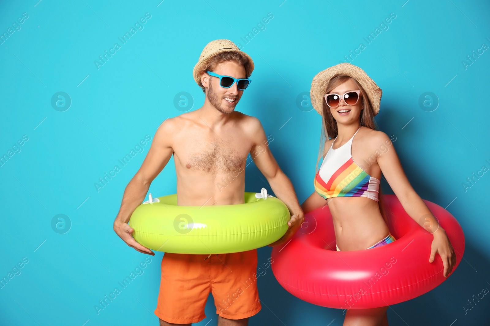 Photo of Young couple in beachwear with inflatable rings on color background