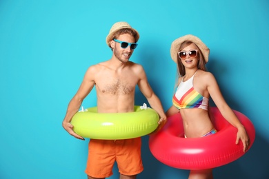 Photo of Young couple in beachwear with inflatable rings on color background