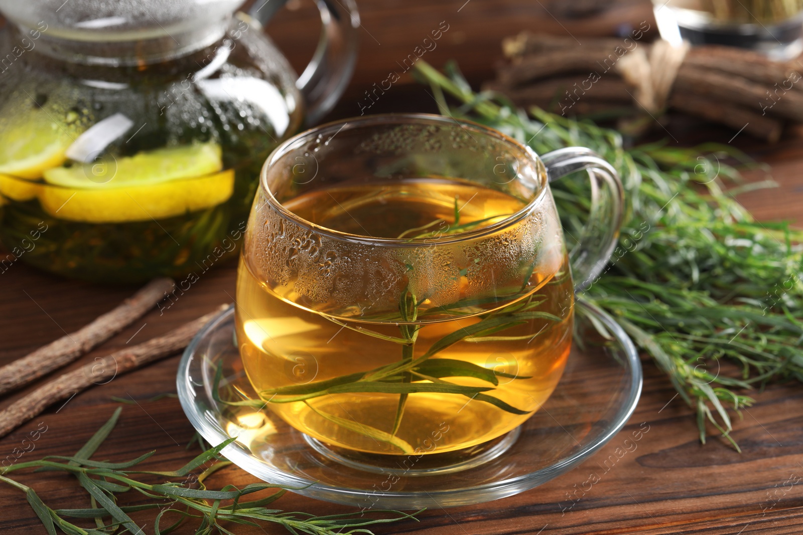 Photo of Homemade herbal tea and fresh tarragon leaves on wooden table, closeup