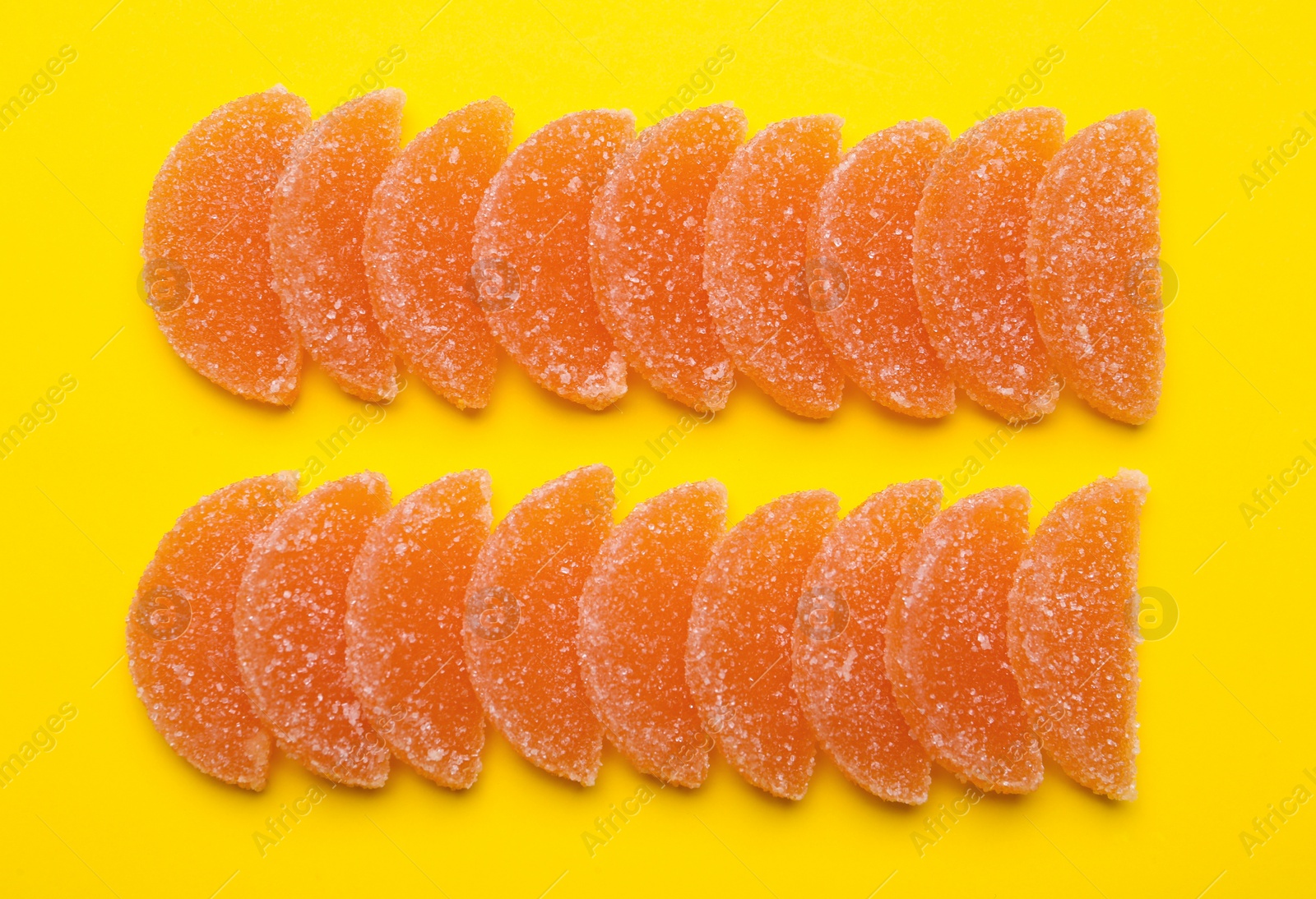 Photo of Delicious orange marmalade candies on yellow background, flat lay