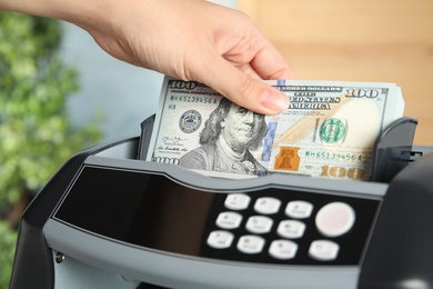 Woman putting money into counting machine indoors, closeup