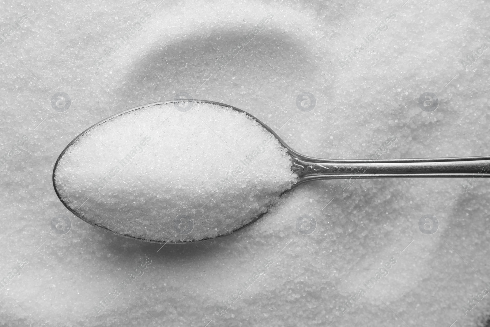 Photo of Metal spoon on granulated sugar, top view