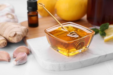 Photo of Cold remedies. Bowl of honey, garlic and syrup on white table, closeup. Cough treatment