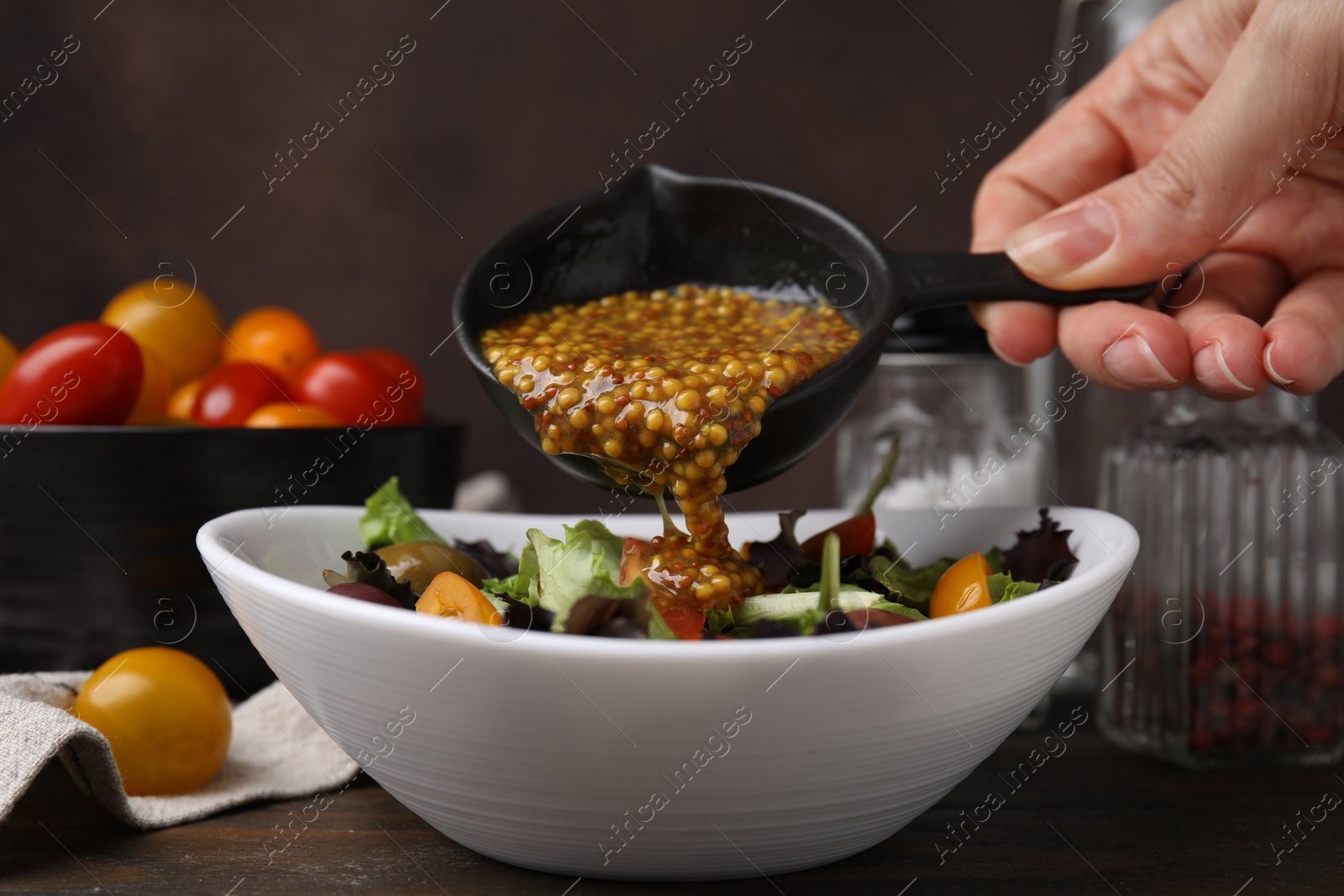 Photo of Woman pouring tasty vinegar based sauce (Vinaigrette) into bowl with salad at wooden table, closeup