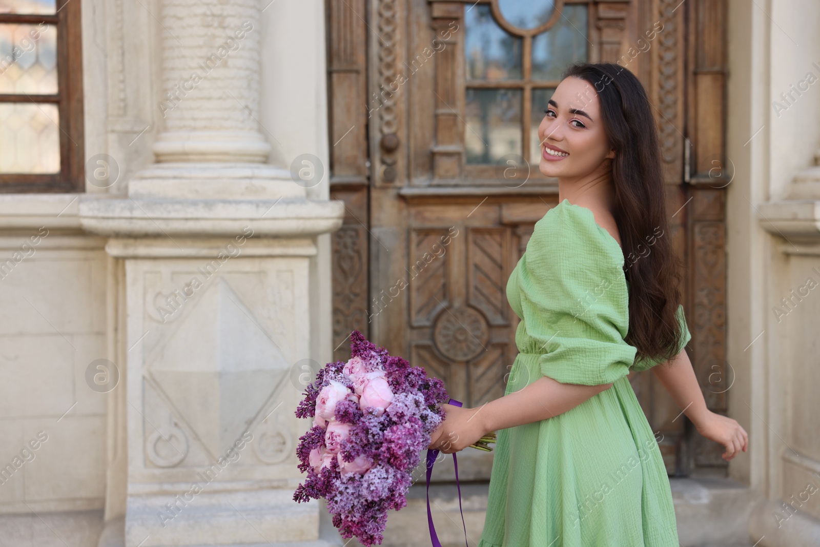 Photo of Beautiful woman with bouquet of spring flowers near building outdoors, space for text