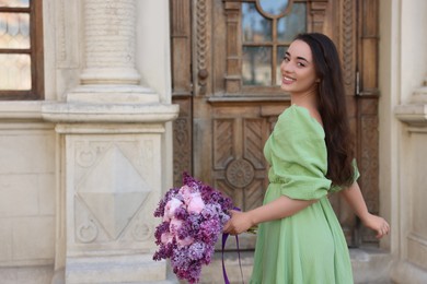 Photo of Beautiful woman with bouquet of spring flowers near building outdoors, space for text