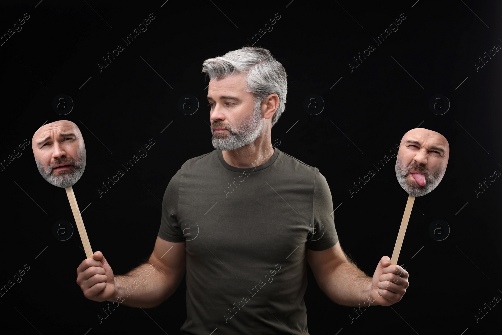 Image of Mature man holding masks with his face showing different emotions on black background. Balanced personality