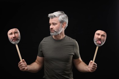 Image of Mature man holding masks with his face showing different emotions on black background. Balanced personality