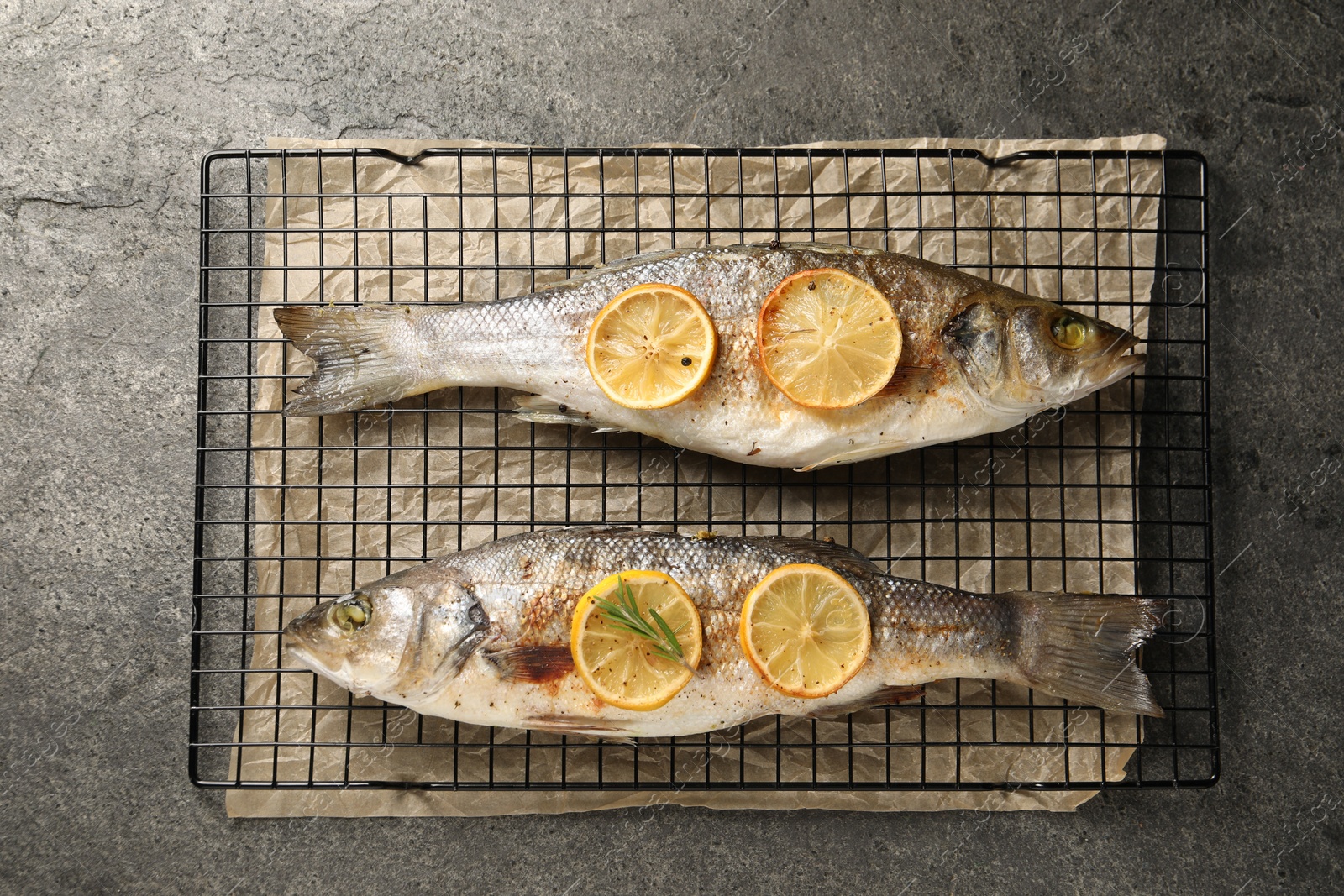 Photo of Baked fish with lemon on grey textured table, top view