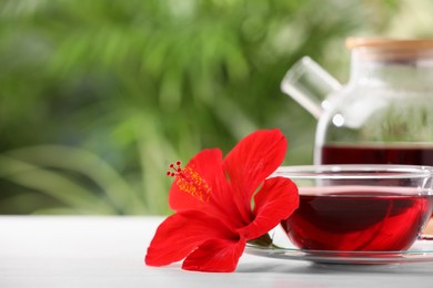 Photo of Delicious hibiscus tea and beautiful flower on white wooden table outdoors, closeup. Space for text