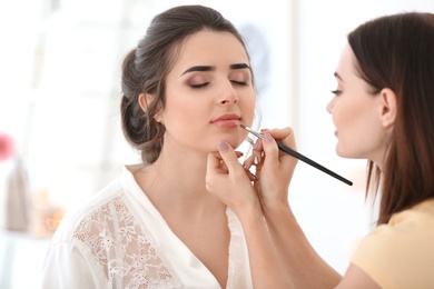 Photo of Professional makeup artist working with young woman in salon