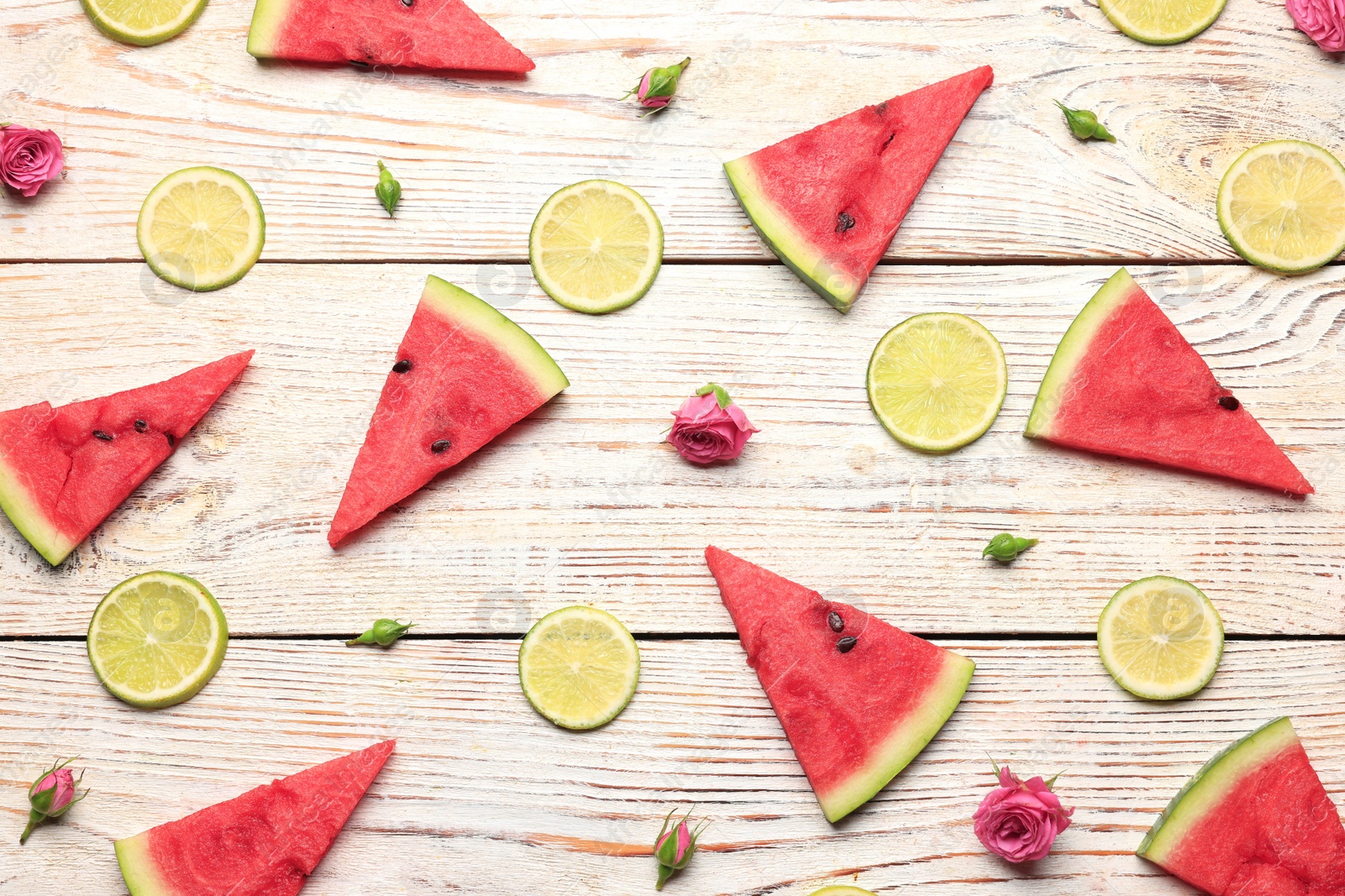 Photo of Tasty sliced watermelon, roses and limes on white wooden table, flat lay