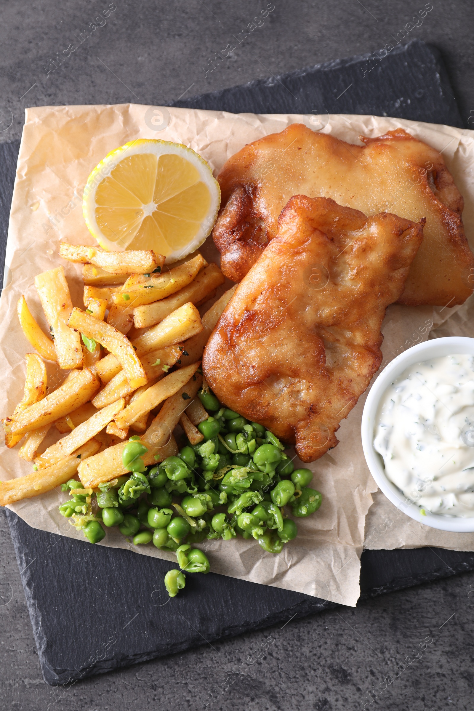 Photo of Tasty fish, chips, sauce and peas on grey table, top view