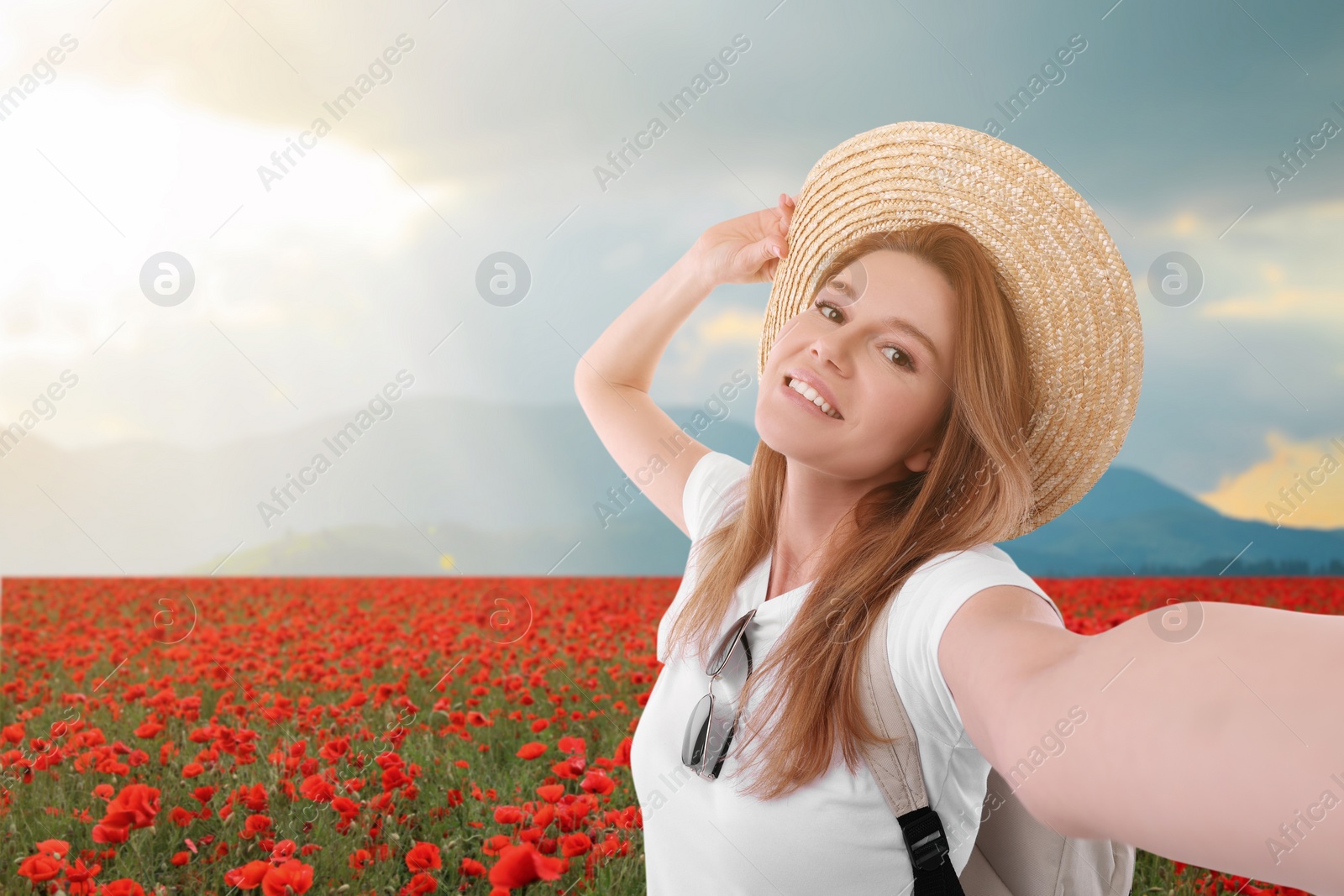 Image of Beautiful woman in straw hat taking selfie in poppy flowers near mountain
