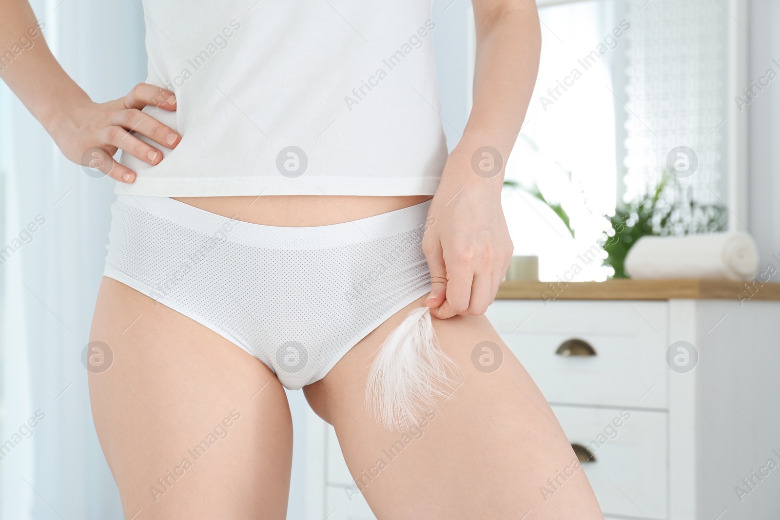 Photo of Young woman touching leg with feather at home, closeup. Epilation procedure