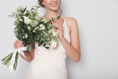 Young bride wearing wedding dress with beautiful bouquet on light grey background, closeup