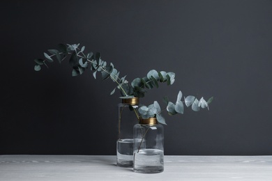 Photo of Beautiful eucalyptus branches in glass vases on white wooden table against black background