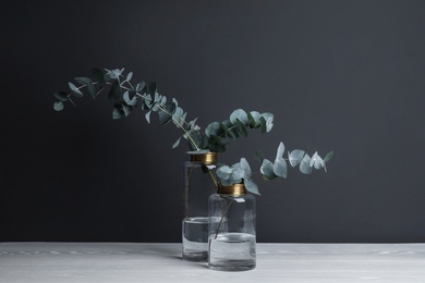 Beautiful eucalyptus branches in glass vases on white wooden table against black background