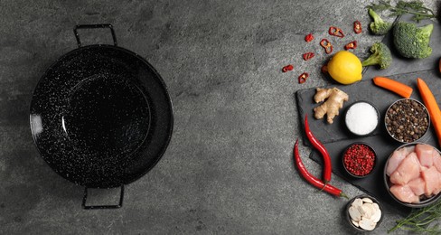 Empty iron wok and raw ingredients on grey table, flat lay. Space for text