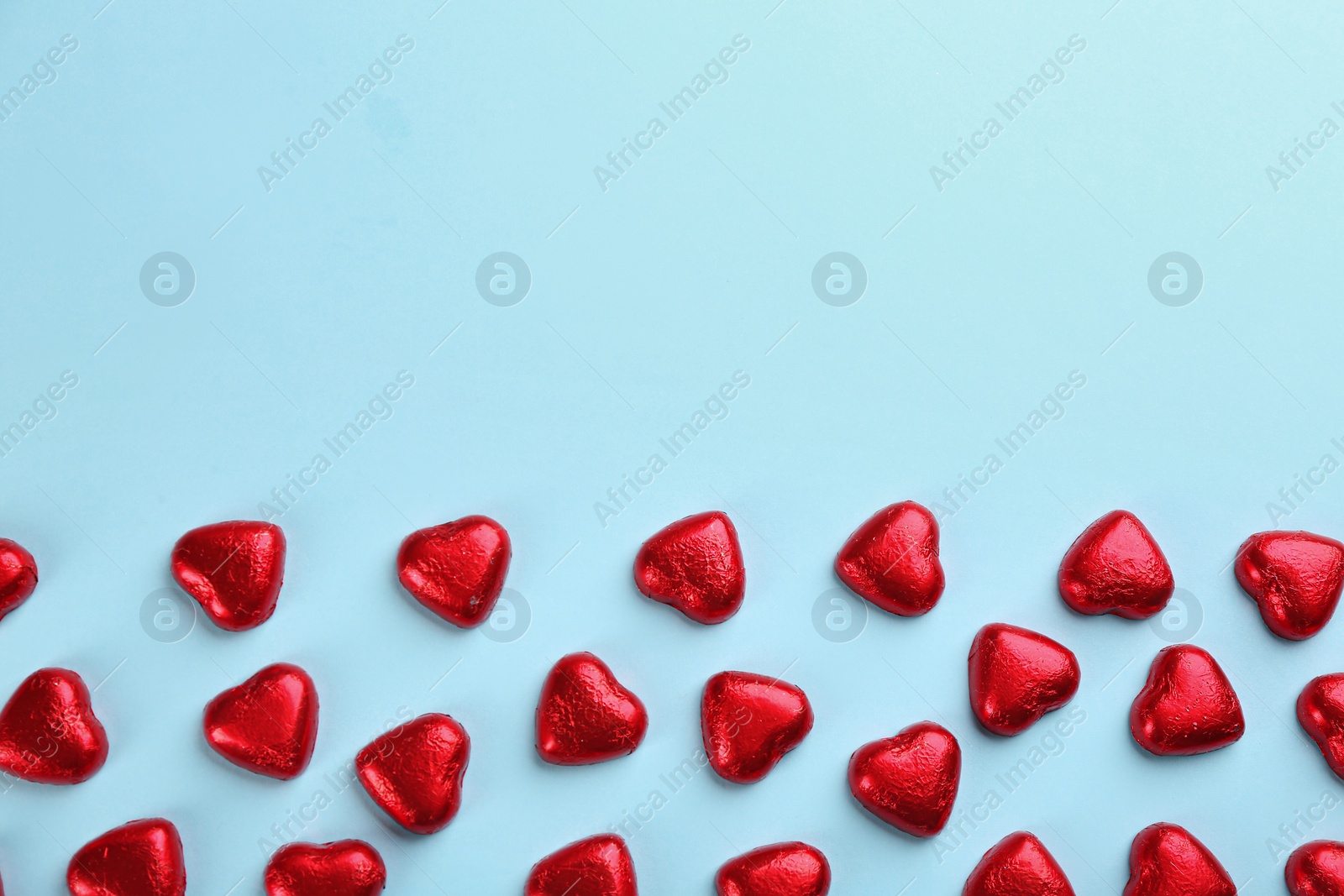 Photo of Heart shaped chocolate candies in red foil on light blue background, flat lay. Space for text