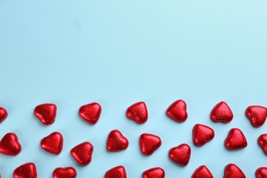 Photo of Heart shaped chocolate candies in red foil on light blue background, flat lay. Space for text