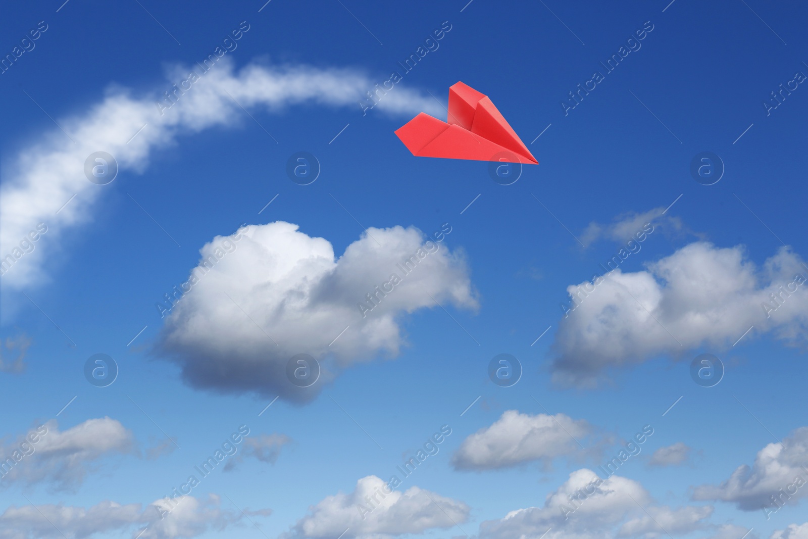 Image of Red paper plane flying in blue sky with clouds