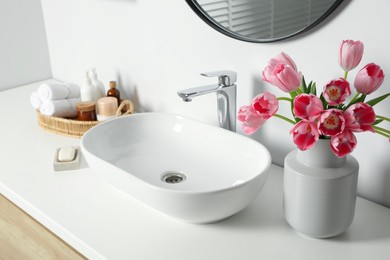 Photo of Vase with beautiful pink tulips and toiletries near sink in bathroom