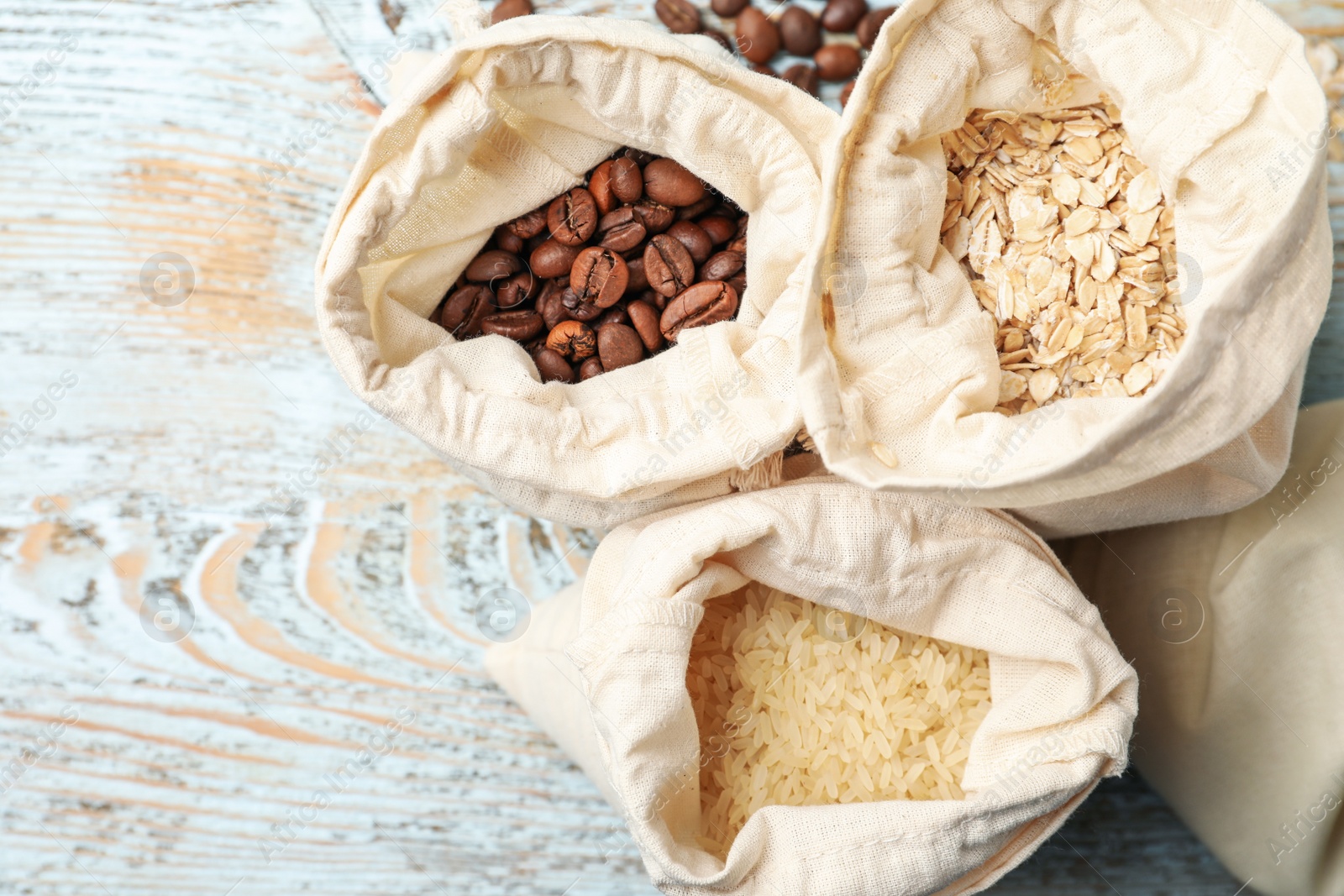 Photo of Cotton eco bags with cereals and coffee beans on wooden table, flat lay