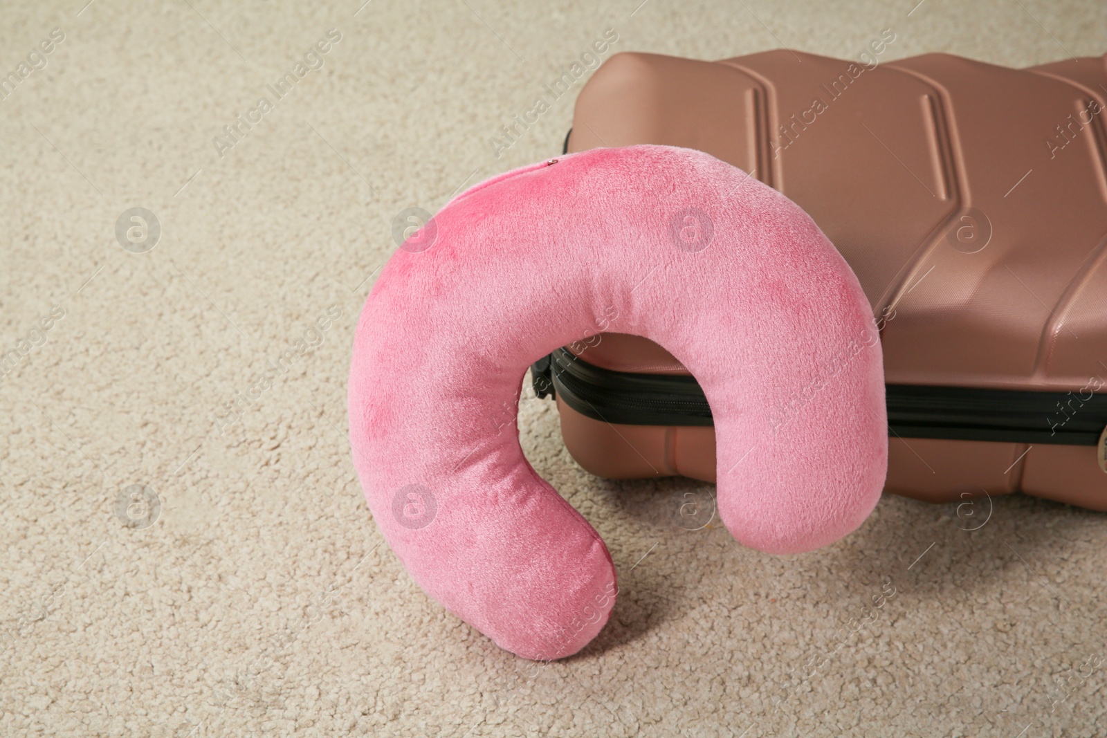 Photo of Pink travel pillow and suitcase on beige rug, space for text