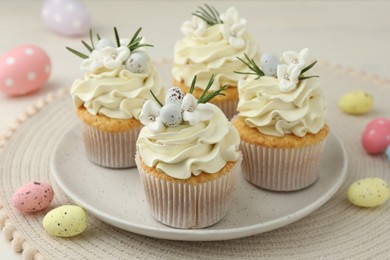 Tasty Easter cupcakes with vanilla cream and candies on table