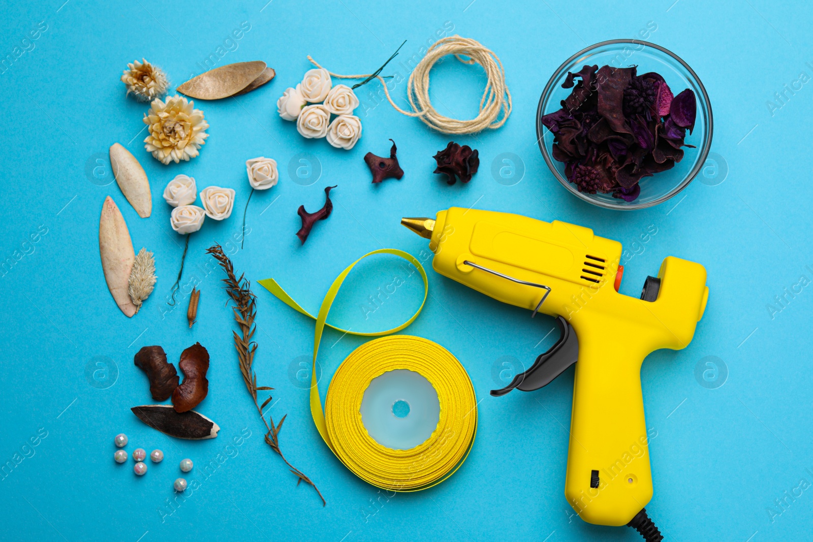 Photo of Hot glue gun and handicraft materials on light blue background, flat lay