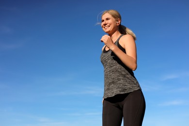 Woman listening to music while running outdoors in morning, low angle view. Space for text