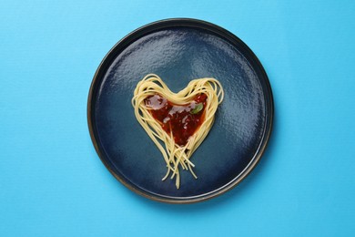 Photo of Heart made with spaghetti and sauce on light blue background, top view