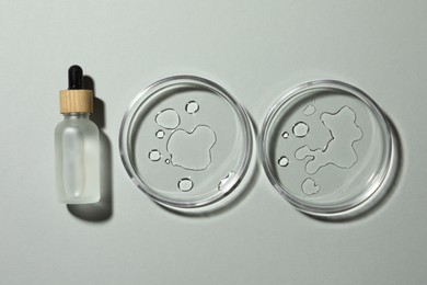 Photo of Petri dishes with sample and bottle on light grey background, flat lay