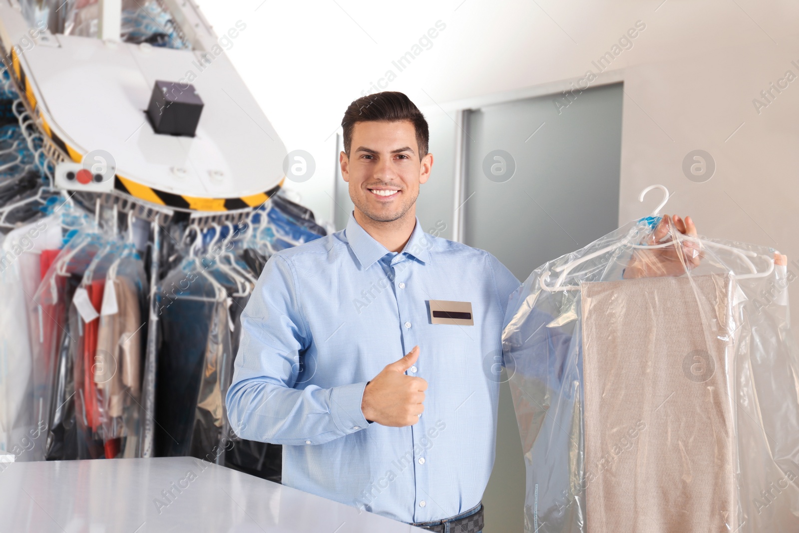 Photo of Portrait of happy worker with clothes near counter at dry-cleaner's