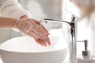 Woman washing hands with soap over sink in bathroom, closeup