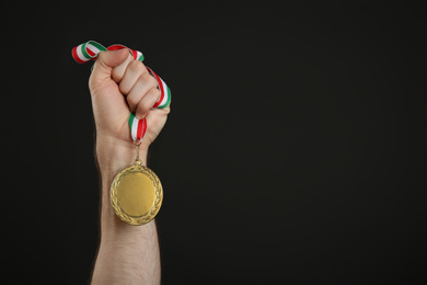 Photo of Man holding golden medal on black background, closeup. Space for design