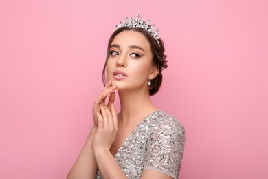 Beautiful young woman wearing luxurious tiara on pink background
