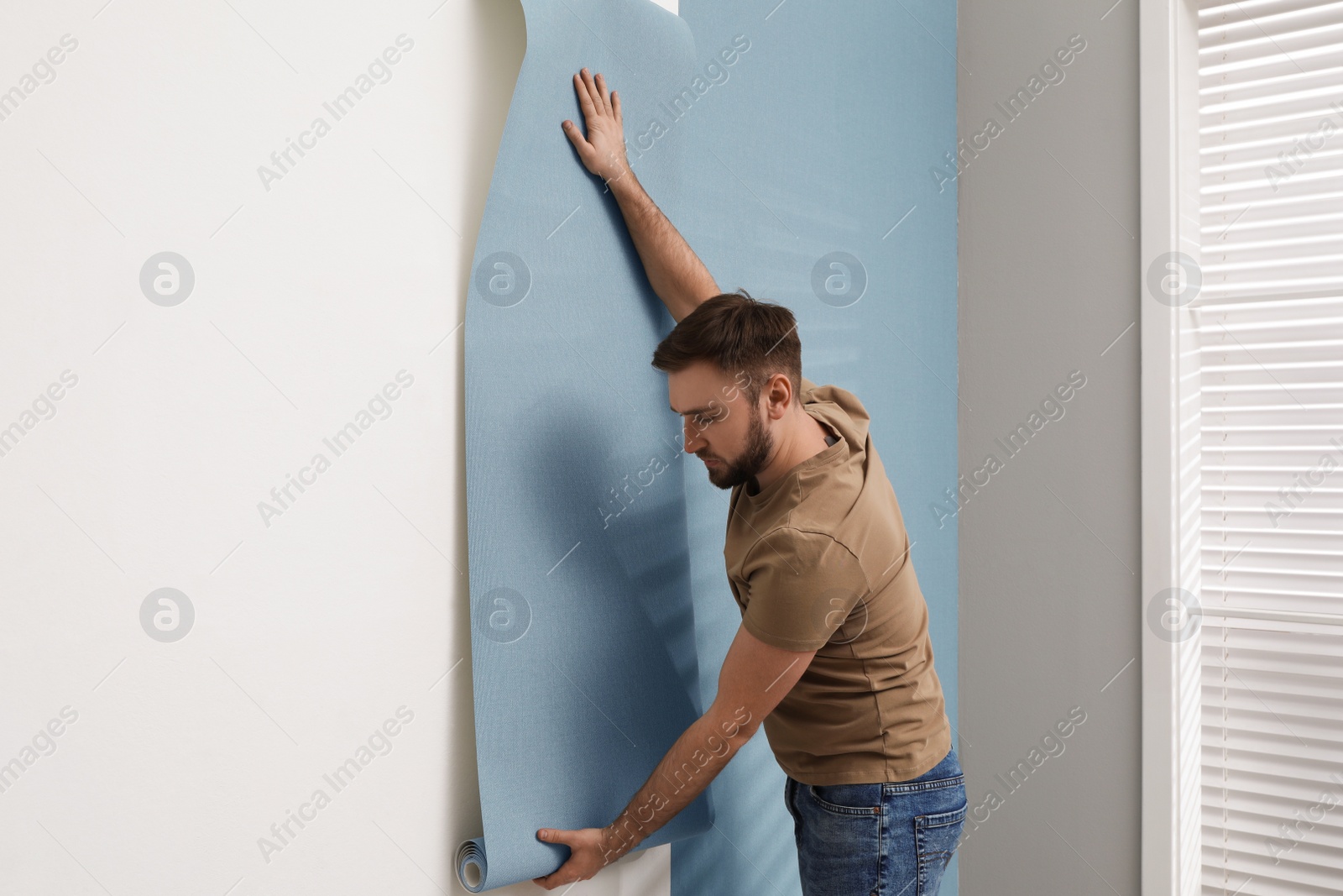 Photo of Man hanging stylish wall paper sheet indoors