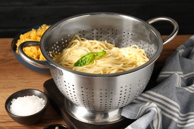 Cooked pasta in metal colander and salt on wooden table, closeup