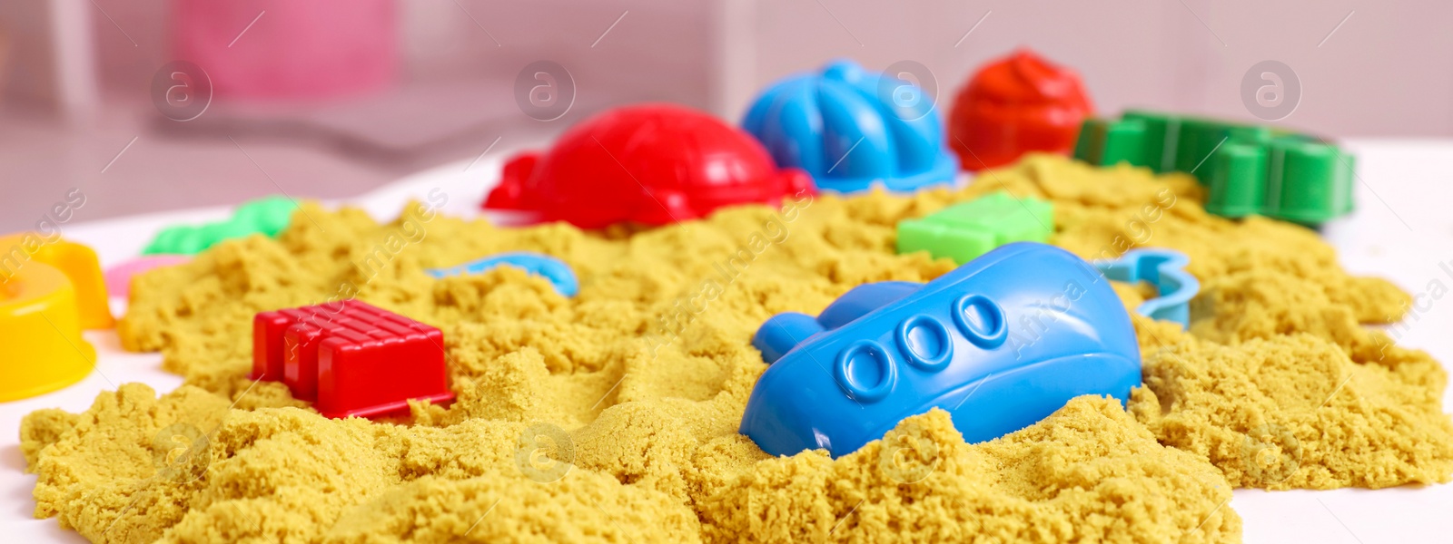 Image of Bright kinetic sand and toys on white table indoors. Banner design