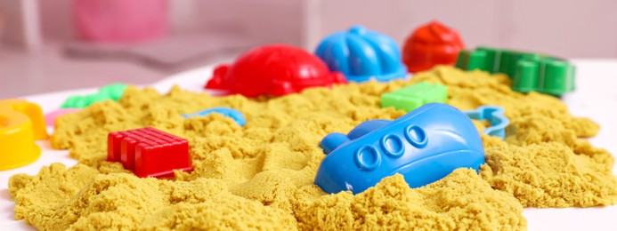 Image of Bright kinetic sand and toys on white table indoors. Banner design