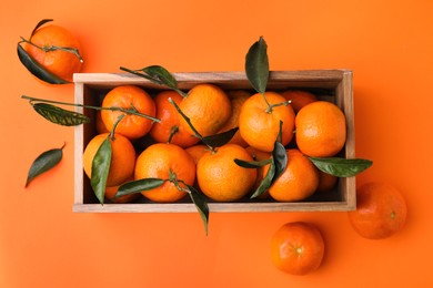 Wooden crate with fresh ripe tangerines and leaves on orange table, flat lay