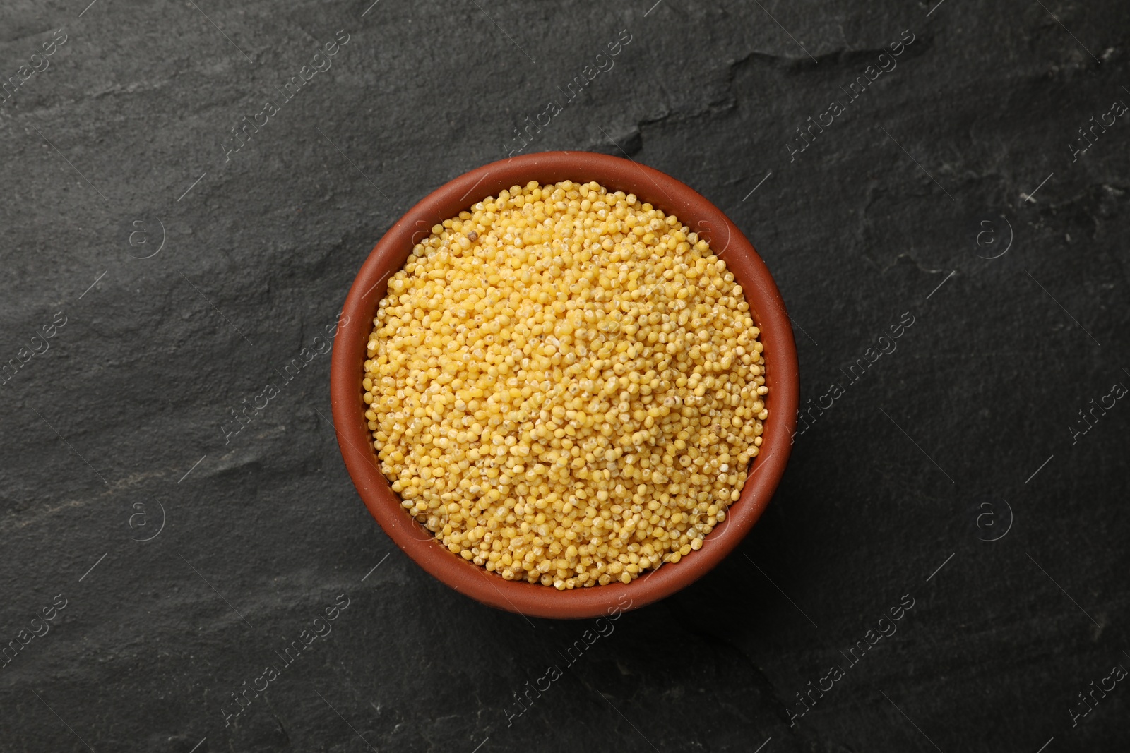 Photo of Millet groats in bowl on black table, top view