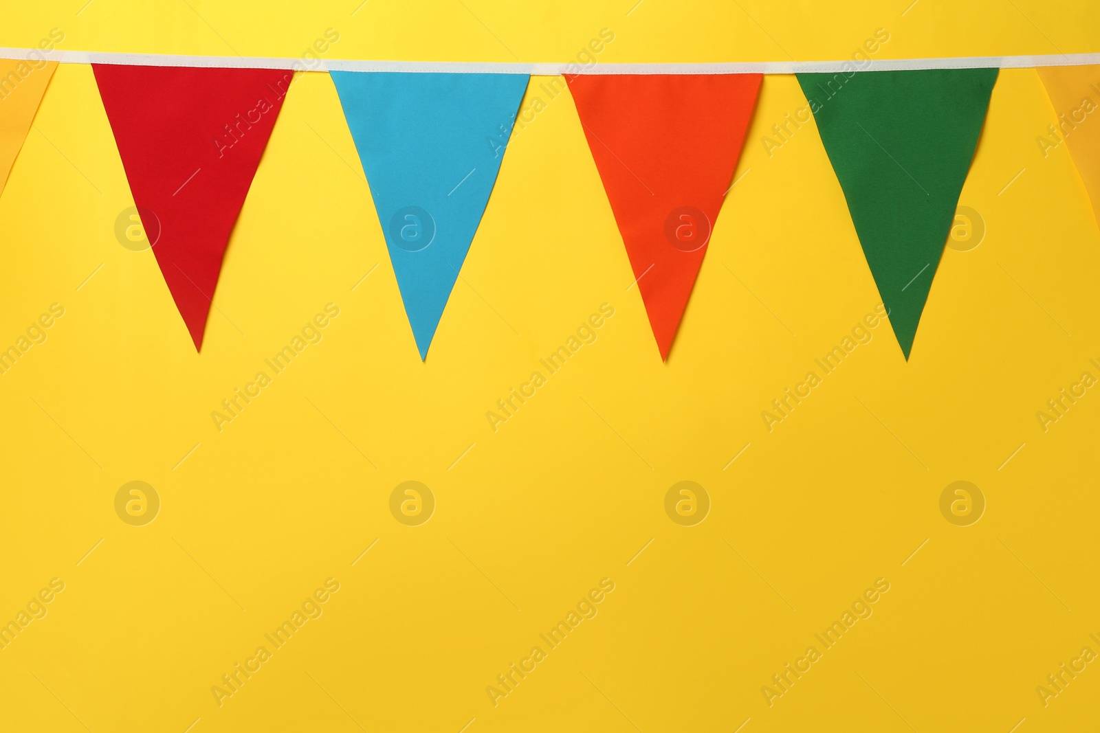 Photo of Bunting with colorful triangular flags on yellow background, space for text